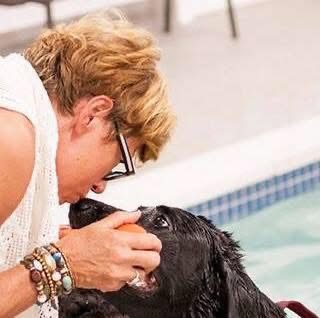 A woman gently caresses a black dog near a pool.